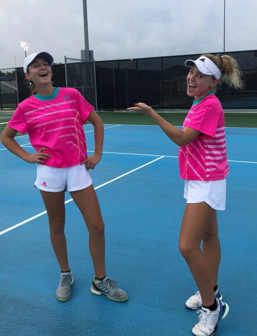 Two female tennis players are standing on a court.