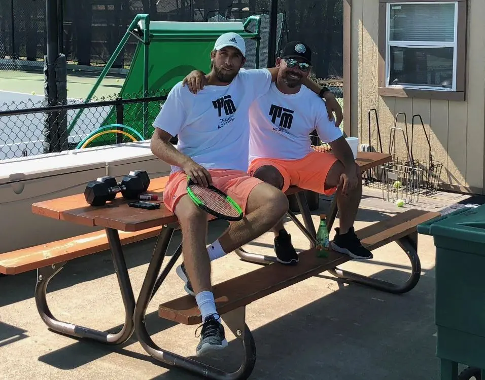 Two men sitting on a bench with tennis shoes.