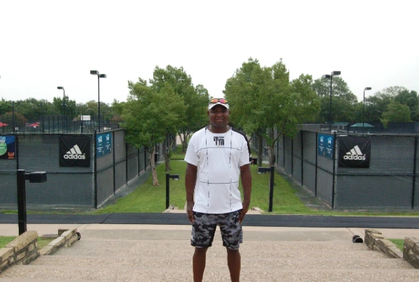A man standing in front of a tennis court.