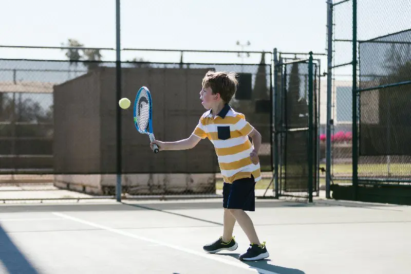 A young boy is playing tennis on the court