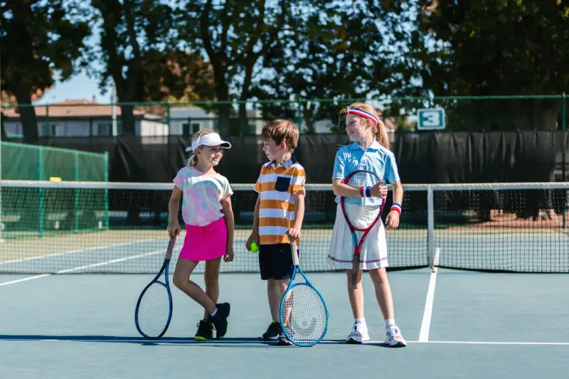 Three children are holding tennis rackets on a court.